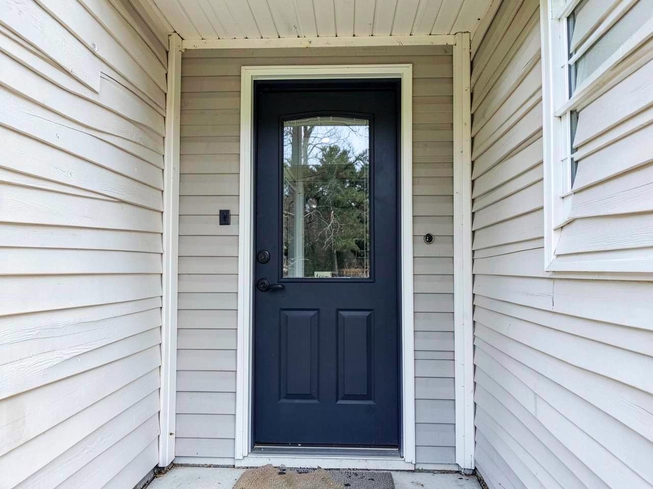 A new dark navy fiberglass entry door with a glass insert on a home with light siding
